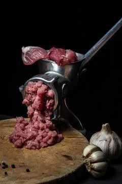Meat in a meat grinder on a black background. Pork meat is twisted in an old mea Stock Photos