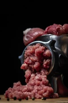 Meat in a meat grinder on a black background. Pork meat is twisted in an old mea Stock Photos