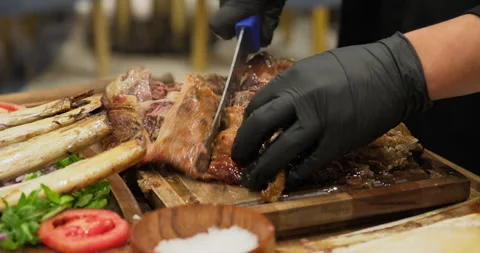 Meat party. Chef cuts soft baked grilled BBQ meat ribs on a wooden board. Meat Stock Footage 291698650