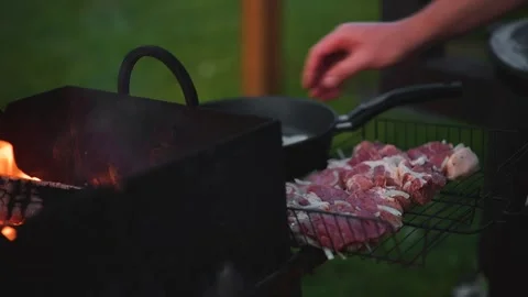 Meat is placed on a grill over a flame in an outdoor area. The flames rise as Stock Footage 345874918