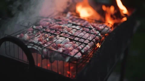 Meat is placed on a grill over flames, producing smoke in an outdoor setting. Stock Footage 345874674