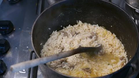 Meat risotto. Rice with pieces of meat in a rustic iron pot. A pot on the stove Fotos de archivo
