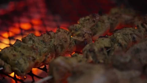 Meat roasting on a grill over glowing hot embers, producing a flame-grilled Stockbeeldmateriaal 304589601