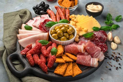Meat snacks of different types, cheese and olives on a dark gray background. Stock Photos