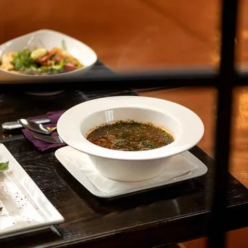 Meat soup with dill on dining table with cutlery on it. View through restaurant Stock-Fotos
