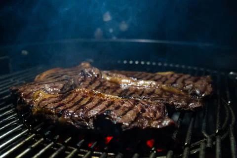 Meat steaks are fried on the grill grill, above it rises smoke from roasted meat Stock Photos