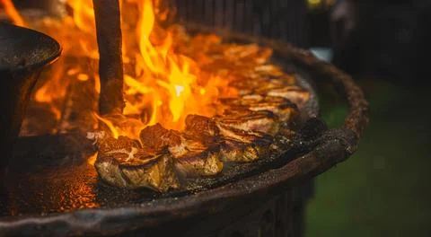 Meat steaks grilling over open fire flames on barbecue grill at night. Cook.. Stock Photos