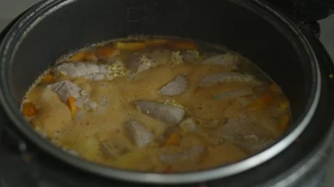 Meat stew with vegetables and grains simmering in multi-cooker Stock Footage 335392087