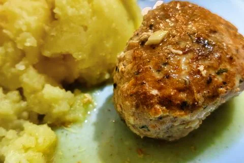 A meatball sits beside a serving of mashed potato on a blue plate. The meal i Stock Photos