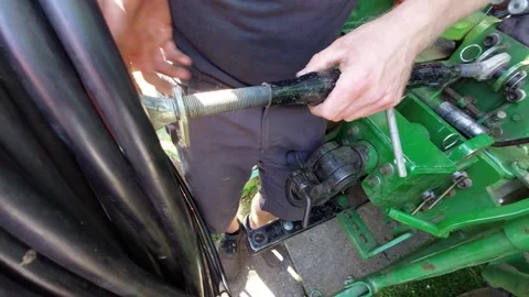 Mechanic adjusting a heavy duty threaded metal rod on a green tractor close up 库存影片 336391381