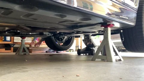 Mechanic Adjusting Jacks Under Car in Garage Stock Footage 136869009