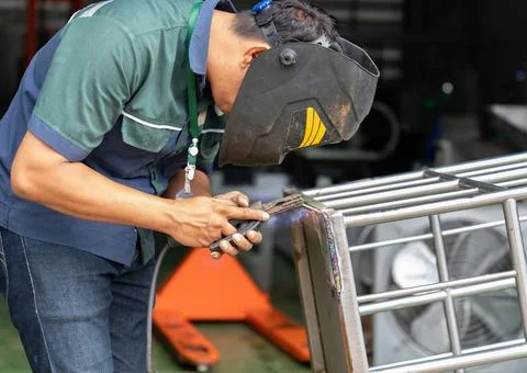 The mechanic bent down to weld the base of the stainless steel wheelchair. Stock Photos