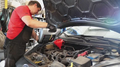 Mechanic in black gloves pours engine oil into a funnel, showcasing the Video stock 347738379