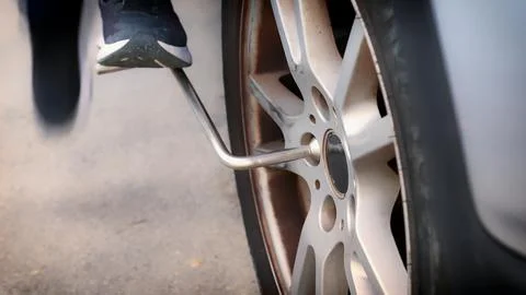 Mechanic changing car tire using wrench and foot pressure Stock Photos