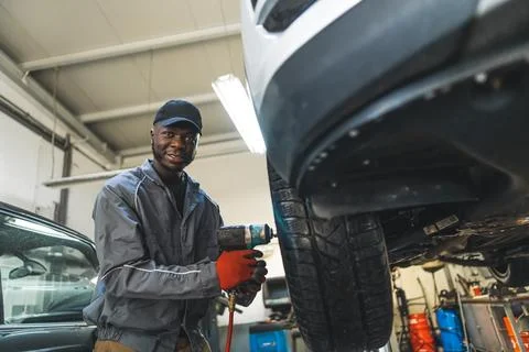 Mechanic changing tyre using an electric wrench car is lifted for smooth process Stock Photos