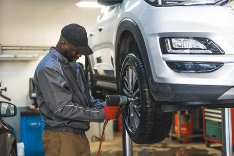 Mechanic changing tyre using an electric wrench car is lifted for smooth process Stock Photos