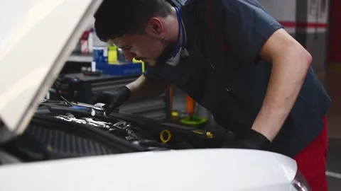 Mechanic checking a car engine and looking with a flashlight in a workshop Stock Footage 132304042
