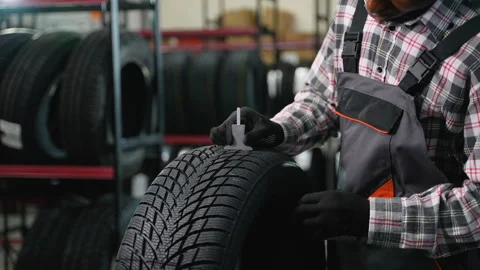 Mechanic checking tire tread depth with gauge in auto shop Stock Footage 301558923