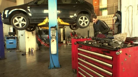 Mechanic with cigarette in month taking off car wheel in garage. Stock Footage 64237472