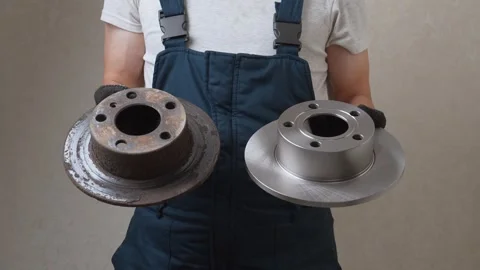 Mechanic comparing old worn brake disc to new one Stock Footage 326142407