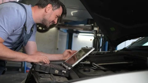 Mechanic diagnosing car problems with laptop in garage Stock Footage 317514637