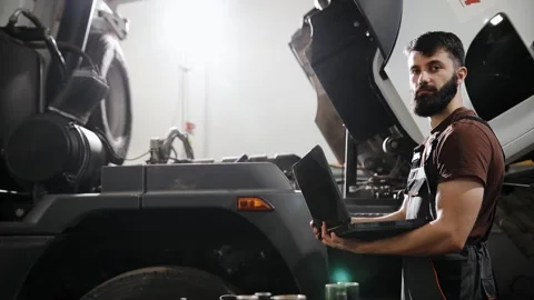 Mechanic diagnosing a truck engine using a laptop in a repair shop, maintenance Stock Footage 333705824