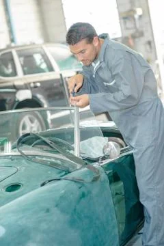 Mechanic doing up screw of windshield on classic car Stock Photos
