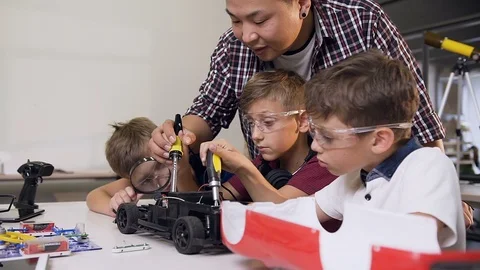 Mechanic engineer helping boys using screwdrivers to assemble robotic machines Video stock 115522352