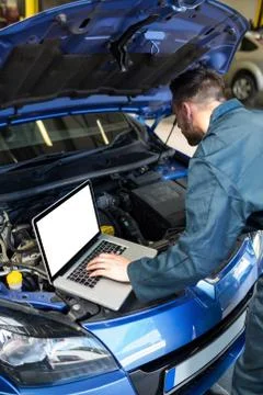 Mechanic examining car engine with help of laptop Stock Photos