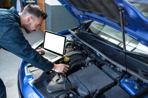 Mechanic examining car engine with help of laptop 库存照片