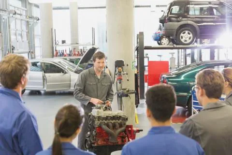 Mechanic explaining car engine to students in auto repair shop Stock Photos