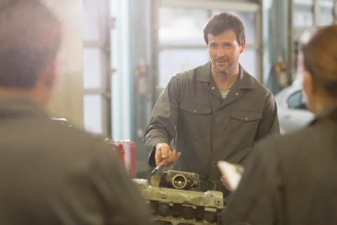 Mechanic explaining engine to students in auto repair shop Stock Photos