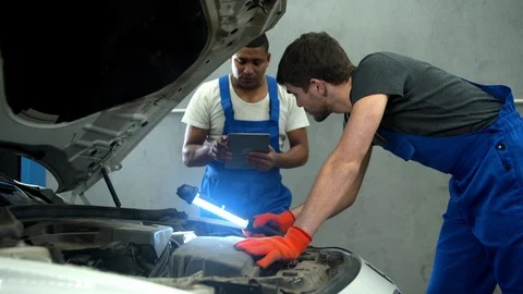 Mechanic with flashlight examines the motor of car and his collegue takes notes Video stock 124264413