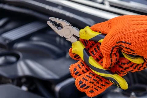A mechanic is focused on fixing a car engine while holding pliers in one ha.. Stock Photos