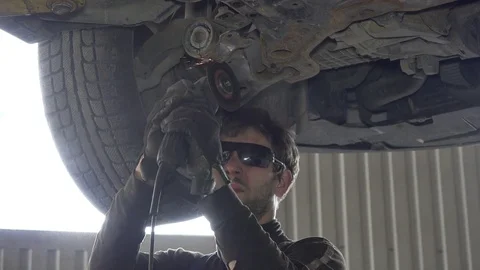 Mechanic guy with glasses cutting worn automobile part with grinder in garage Stock Footage 70173626