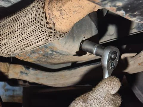 Mechanic hand in a glove using a socket wrench to loosen an oil drain plug from Stock Photos