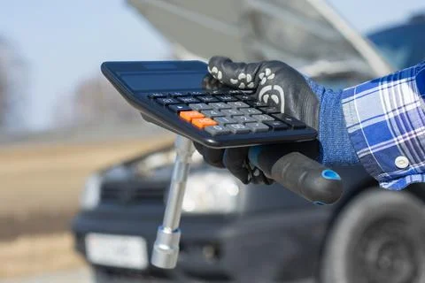 Mechanic hand using calculator while holding wrench near car, representing .. Stock Photos