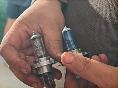Mechanic hands holding and comparing two automotive halogen headlight bulbs, a Stock Photos
