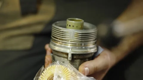 Mechanic holds a dirty car engine oil filter housing cover Stock Footage 337569020