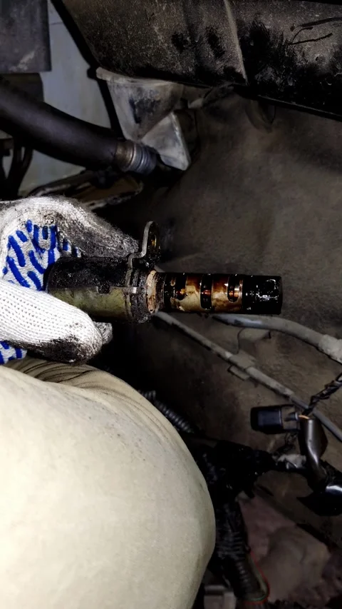 A mechanic holds a dirty car variable valve timing solenoid valve. Video stock 338364908