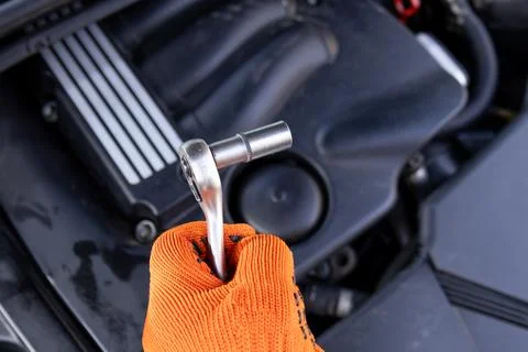 A mechanic holds a ratchet tool while working on a car engine in a garage. .. Stock Photos