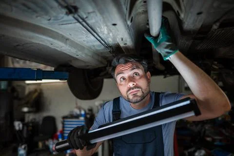 Mechanic inspecting car chassis using led work light in garage Stock Photos