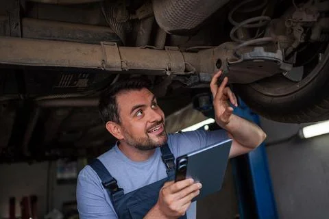 Mechanic inspecting car chassis using digital tablet in auto repair shop Stock Photos