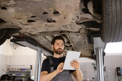 Mechanic inspecting car undercarriage using tablet 스톡 사진