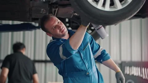 Mechanic inspects car underside with focused expression 库存影片 345031589