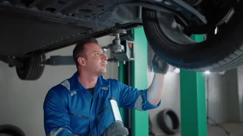 Mechanic inspects EV car under lift, focused and precise Stock Footage 338332405