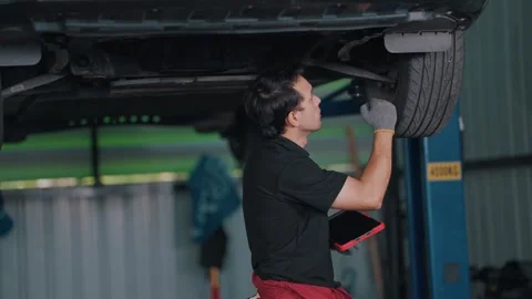 Mechanic inspects EV car under lift with focused gaze Stock-Footage 341461874