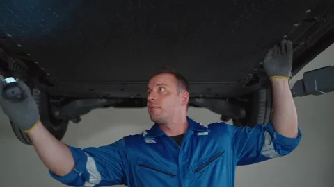 Mechanic inspects EV car underside with flashlight 库存影片 338332400