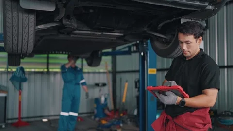 Mechanic inspects EV car underside with tablet Stock-Footage 341461432