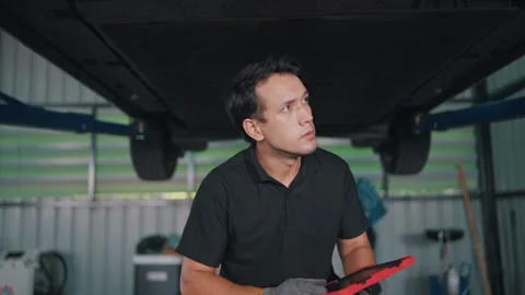Mechanic inspects EV car underside under lift Stock-Footage 341461486